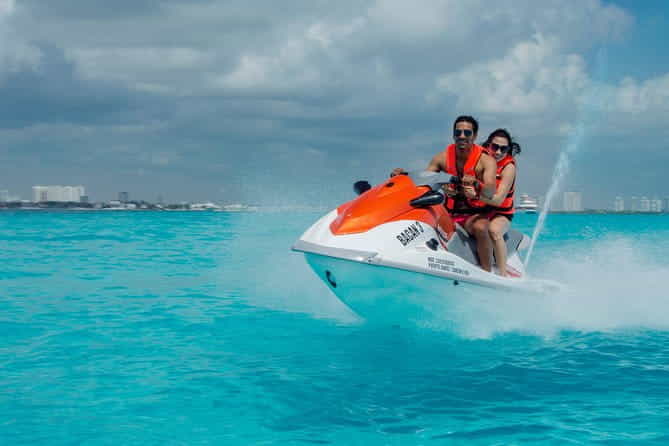 Two people in life vests riding a white and orange wave runner on bright turquoise waters in Cancun